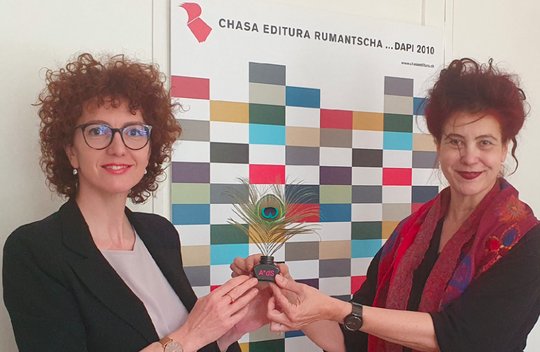 «Mit dem dezidierten Charme einer ‘valerusa da Lumnezia’»: Fabiola Carigiet (r.) überreicht Anita Capaul die «Plume de paon». (Bild zVg)